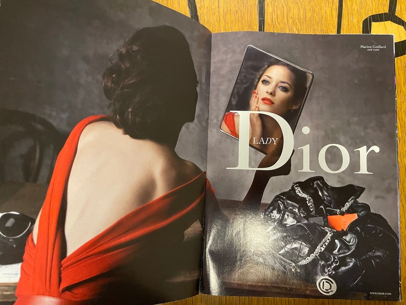 May include: A woman in a red dress looks into a mirror, the reflection shows a woman with red lipstick and the text "Lady Dior".