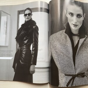 May include: Two women wearing different styles of jackets. The woman on the left is wearing a black leather jacket with a fur collar and a belt. The woman on the right is wearing a gray tweed jacket with a black ribbon tied at the waist.