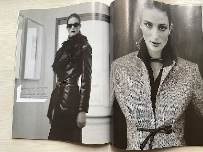 May include: Two women wearing different styles of jackets. The woman on the left is wearing a black leather jacket with a fur collar and a belt. The woman on the right is wearing a gray tweed jacket with a black ribbon tied at the waist.
