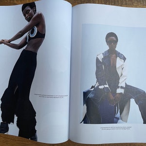 Puede incluir: Dos modelos de moda posan en un editorial de revista. La modelo de la izquierda lleva una falda negra con un dobladillo con volantes y un top negro y azul. La modelo de la derecha lleva una chaqueta blanca y azul con un top negro y unos vaqueros azules.