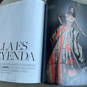Puede incluir: Una p&aacute;gina de revista de moda con una modelo luciendo un vestido vibrante y estampado. El vestido combina elementos rojos, azules y dorados. El texto "ELLA ES LEYENDA" es visible en la p&aacute;gina adyacente.