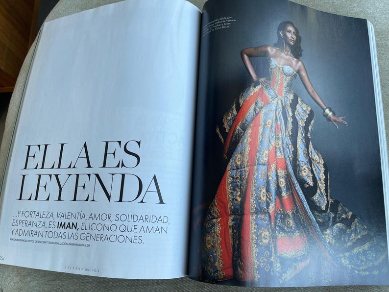 Puede incluir: Una p&aacute;gina de revista de moda con una modelo luciendo un vestido vibrante y estampado. El vestido combina elementos rojos, azules y dorados. El texto "ELLA ES LEYENDA" es visible en la p&aacute;gina adyacente.