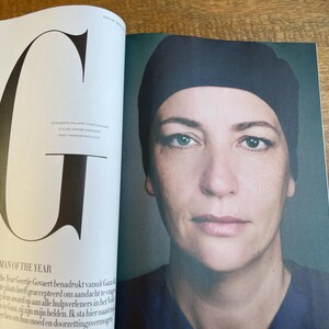 May include: A magazine spread featuring a portrait of a woman wearing a dark blue cap. The text "WOMAN OF THE YEAR" is visible, along with a large letter "G". The image is set against a neutral background.