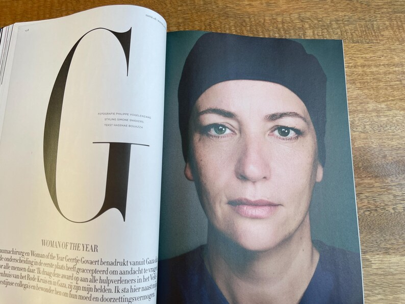 May include: A magazine spread featuring a portrait of a woman wearing a dark blue cap. The text "WOMAN OF THE YEAR" is visible, along with a large letter "G". The image is set against a neutral background.