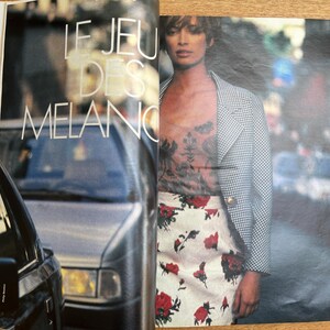 May include: A fashion magazine spread featuring a woman in a checkered blazer, floral top, and a white skirt with red rose patterns. The text "LE JEU DES MELAN" is visible. A man is seen in the background.