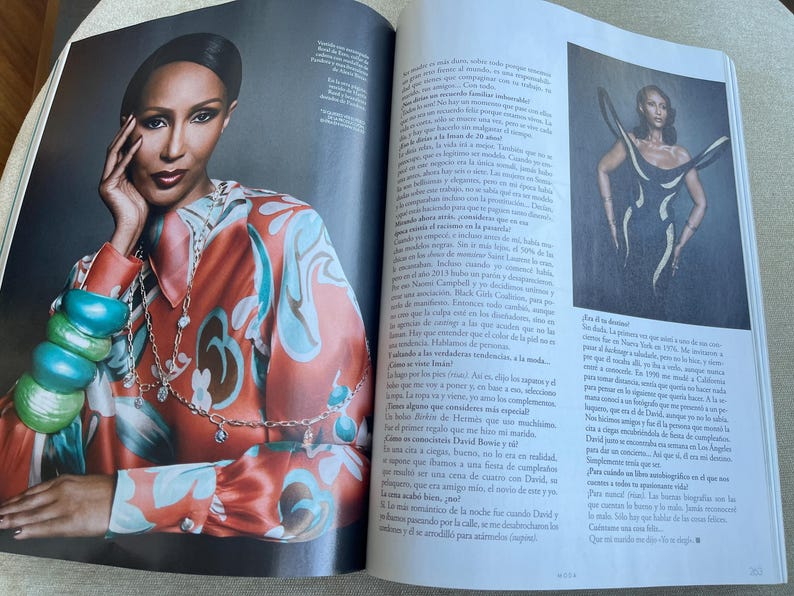 Puede incluir: Una foto de revista con una mujer que lleva una camisa de seda estampada en tonos naranja, turquesa y marr&oacute;n. Est&aacute; adornada con collares superpuestos y pulseras gruesas. La imagen forma parte de un art&iacute;culo de revista.