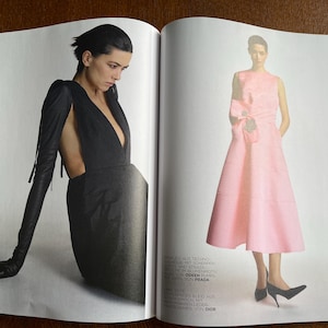 Puede incluir: Una doble p&aacute;gina de una revista de moda. Una modelo lleva un vestido negro con guantes largos y un escote pronunciado. La otra modelo viste un vestido rosa sin mangas con un lazo y tacones negros.