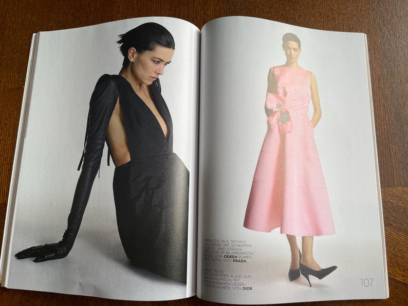 Puede incluir: Una doble p&aacute;gina de una revista de moda. Una modelo lleva un vestido negro con guantes largos y un escote pronunciado. La otra modelo viste un vestido rosa sin mangas con un lazo y tacones negros.