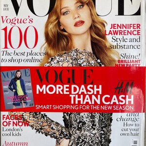 Può includere: Un numero di novembre della rivista Vogue con Jennifer Lawrence in copertina. La copertina mostra il testo Vogue, 100, Jennifer Lawrence Style and substance, More Dash Than Cash e H&M. Il soggetto indossa un capo in pizzo bianco e nero.