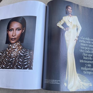 Puede incluir: Una revista con un retrato y una foto de cuerpo entero. El retrato muestra a una persona con cabello oscuro y un collar de joyas. La foto de cuerpo entero muestra a una persona con un vestido largo color crema. Texto en espa&ntilde;ol visible.