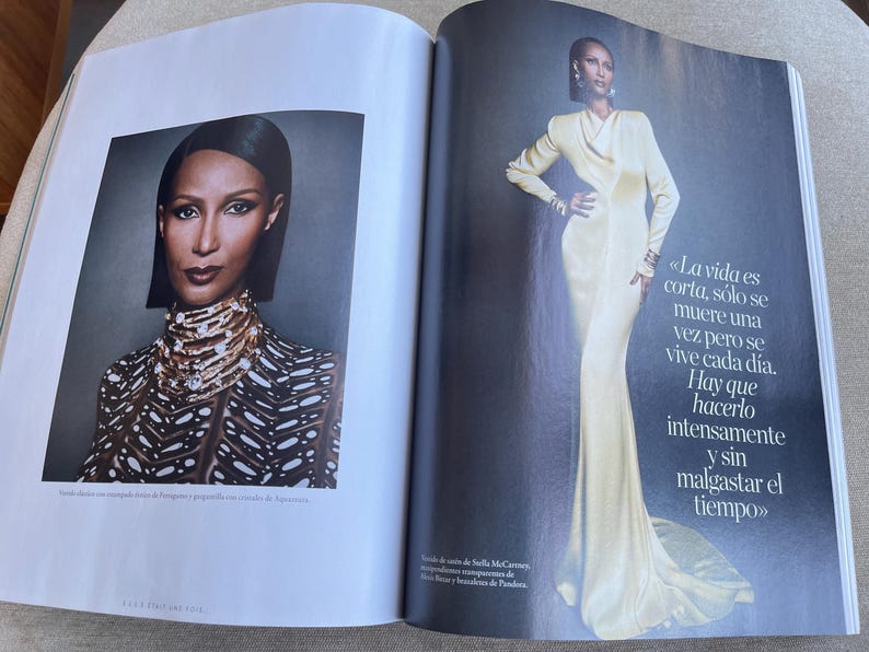 Puede incluir: Una revista con un retrato y una foto de cuerpo entero. El retrato muestra a una persona con cabello oscuro y un collar de joyas. La foto de cuerpo entero muestra a una persona con un vestido largo color crema. Texto en espa&ntilde;ol visible.