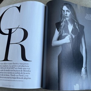 Puede incluir: Una revista con una fotograf&iacute;a en blanco y negro de una mujer con un vestido oscuro. La p&aacute;gina izquierda muestra las letras grandes "C" y "R" en negro. Texto en espa&ntilde;ol que describe a Camille Razart.