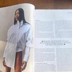 May include: A magazine photograph showing a woman in a white shirt. The shirt is large and asymmetrical. The magazine pages include text and the word "Interview".