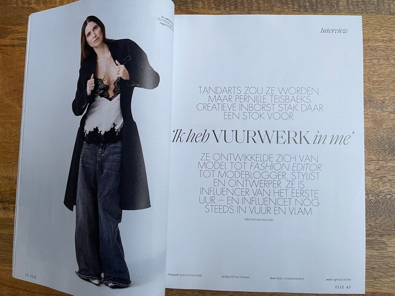 Puede incluir: Una mujer con un abrigo negro sobre una blusa de encaje blanca y pantalones vaqueros azules. El texto de la imagen dice "Tandarts zou ze worden, maar Pernille Teisbaeks creatieve inborst stak daar een stok voor. 'Ik heb vuurwerk in me'".