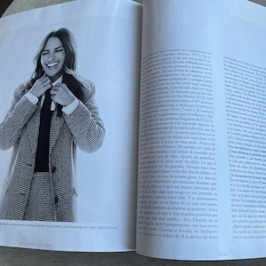 Puede incluir: Fotograf&iacute;a en blanco y negro de una mujer con un traje de pata de gallo, camisa blanca y corbata negra, sonriendo y ajust&aacute;ndose la corbata. La imagen es de una revista, con texto visible en las p&aacute;ginas circundantes.