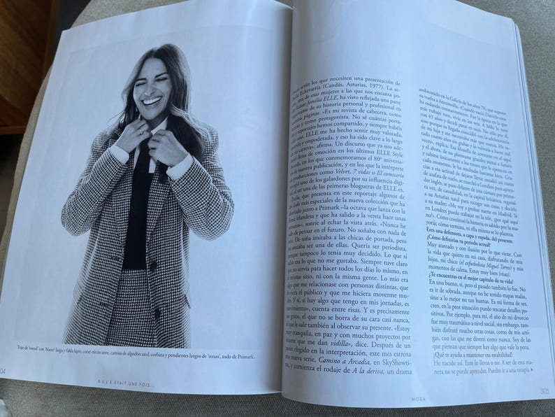 Puede incluir: Fotograf&iacute;a en blanco y negro de una mujer con un traje de pata de gallo, camisa blanca y corbata negra, sonriendo y ajust&aacute;ndose la corbata. La imagen es de una revista, con texto visible en las p&aacute;ginas circundantes.