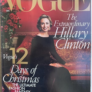 Può includere: Un numero di dicembre della rivista Vogue con Hillary Clinton in copertina. La copertina mostra il testo Vogue, The Extraordinary Hillary Clinton e Vogue's 12 Days of Christmas The Ultimate Fashion Fantasy. Lo sfondo è rosso.