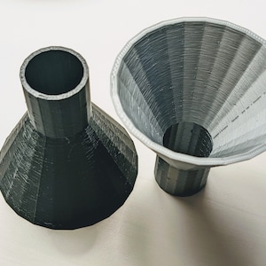 May include: Two 3D printed funnels, one black and one gray. The funnels are made of a textured plastic and have a wide opening at the top and a narrow opening at the bottom.