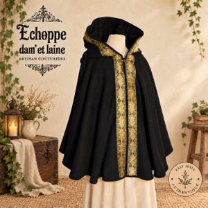 May include: A black hooded cloak featuring a wide, ornate gold and blue patterned trim along the front opening and hood edge. The cloak is secured at the neck with a decorative metal clasp. Text on the image reads Echoppe dam'et laine.