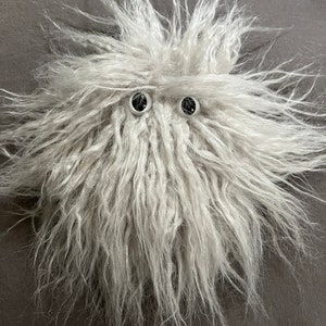 May include: A fluffy white toy with two black eyes. The toy is made of soft, fuzzy material and has a whimsical appearance.