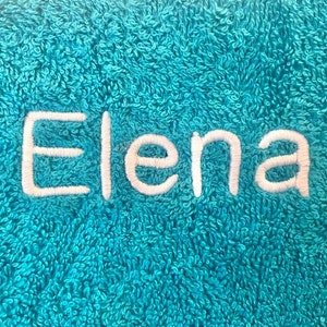 Pu&ograve; includere: Un asciugamano blu turchese con il nome "Elena" ricamato in filo bianco.