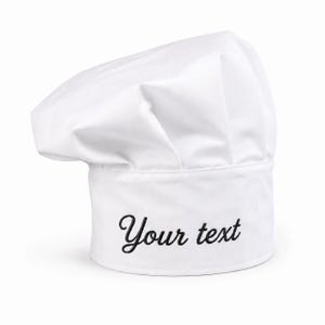 May include: A white chef hat featuring a tall, pleated crown and a structured band. The front of the band is embroidered with the black text "Your text" in a cursive script font. The hat is made of a smooth, opaque fabric with a clean finish.