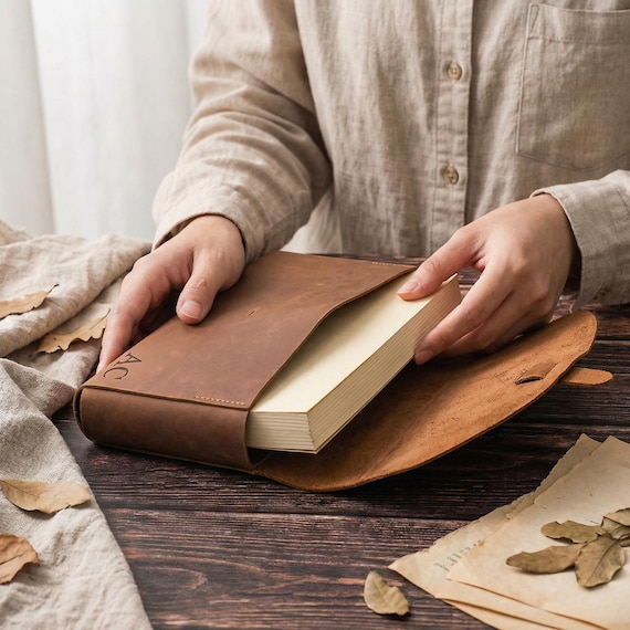 A monogrammed leather sleeve that protects your book like a proper artifact — a genuinely thoughtful gift for the reader who treats their books like treasures.