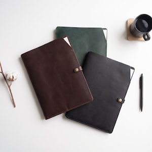 May include: Three rectangular leather document folders in dark brown, forest green, and black. Each folder features a smooth matte finish, a single brass-coloured metal snap button closure on the side, and a slim profile designed to hold paper documents.