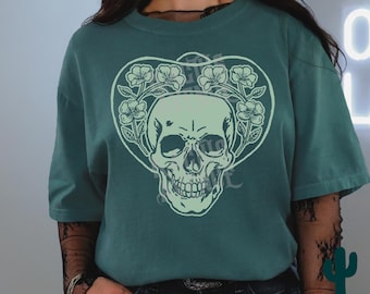 May include: A teal green t-shirt with a white skull design. The skull is surrounded by a floral wreath with white flowers.
