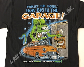 Könnte beinhalten: Schwarzes T-Shirt mit einer Cartoon-Illustration eines grünen Monsters, das einen Schraubenschlüssel hält und vor einem Auto steht. Der Text auf dem Shirt lautet "Vergiss das Haus! Wie groß ist die Garage!"
