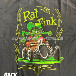 May include: Black fabric with a graphic of Rat Fink driving a hot rod. The cartoon character is green with red accents, and the car is brown. The text "Rat Fink" is in neon green, with the word "BACK" in white at the bottom.