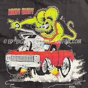 May include: A black t-shirt with a cartoon illustration of a green monster driving a red pickup truck with the words "Heavy Chevy" printed on the shirt. The monster is holding a pool cue with a billiard ball on the end. The truck has flames coming out of the exhaust pipes. The words "BACK" and "ED "BIG" DAD" are printed on the shirt.