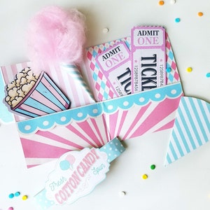 May include: A pink and blue paper craft box with a popcorn bucket, cotton candy, and tickets that say "Admit One" and "Tickle Me".