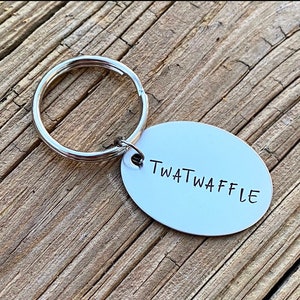 May include: A silver key chain with a round metal tag that says "TWATWAFFLE" in black lettering.