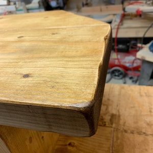 Puede incluir: Primer plano de una mesa de madera r&uacute;stica con borde natural. La tapa es de color marr&oacute;n claro con vetas y nudos de madera visibles. Los bordes son de color marr&oacute;n oscuro y la mesa parece hecha a mano.