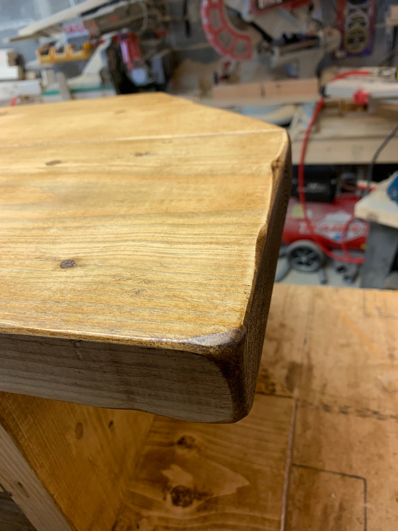 Puede incluir: Primer plano de una mesa de madera r&uacute;stica con borde natural. La tapa es de color marr&oacute;n claro con vetas y nudos de madera visibles. Los bordes son de color marr&oacute;n oscuro y la mesa parece hecha a mano.