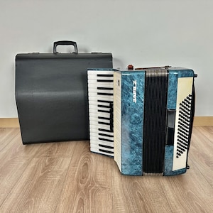Op de afbeelding: Een blauw en zwart accordeon met een wit toetsenbord en een zwarte draagtas. Het accordeon heeft een getextureerd blauw oppervlak en een wit en zwart patroon. De draagtas is zwart en heeft een handvat.