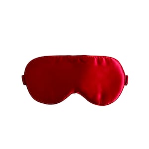 Peut inclure: Un masque de sommeil en satin rouge uni. Le masque est de forme ovale avec un bord inférieur incurvé et une texture lisse et brillante. Il possède une bande de chaque côté pour l'attacher. Le fond est blanc uni.