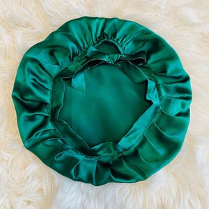 Puede incluir: Una gorro de dormir de satén verde oscuro con la parte superior fruncida y un lazo en la parte posterior.