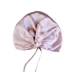 Puede incluir: Un turbante de satén rosa con un diseño anudado y una larga corbata.