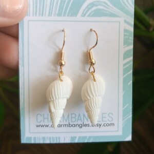 May include: White seashell earrings with gold hooks. The earrings are displayed on a white card with the text "Charm Bangles" and "www.charmbangles.etsy.com".