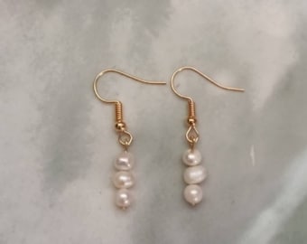 May include: A pair of gold dangle earrings with three white pearl beads on each earring.