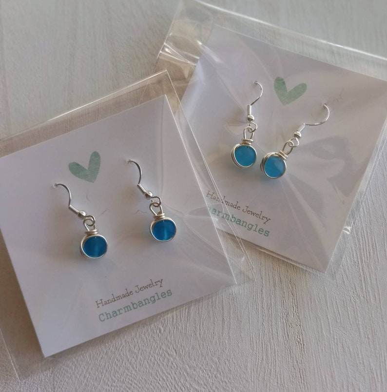 May include: Two pairs of silver dangle earrings with blue glass beads. The earrings are packaged on white cards with the text "Handmade Jewelry Charmbangles".