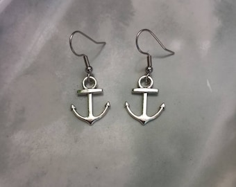 May include: A pair of silver anchor earrings with a simple design. The earrings are on a white surface.