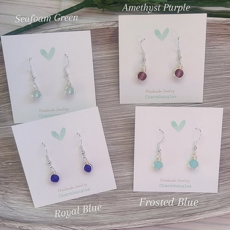May include: Four pairs of handmade earrings with different colored glass beads. The colors are seafoam green, amethyst purple, royal blue, and frosted blue. Each pair is displayed on a white card with the color name and "Handmade Jewelry Charmbangles" written on it.