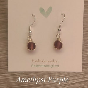May include: Amethyst purple earrings with silver hooks and gold wire wrapped around the stone.