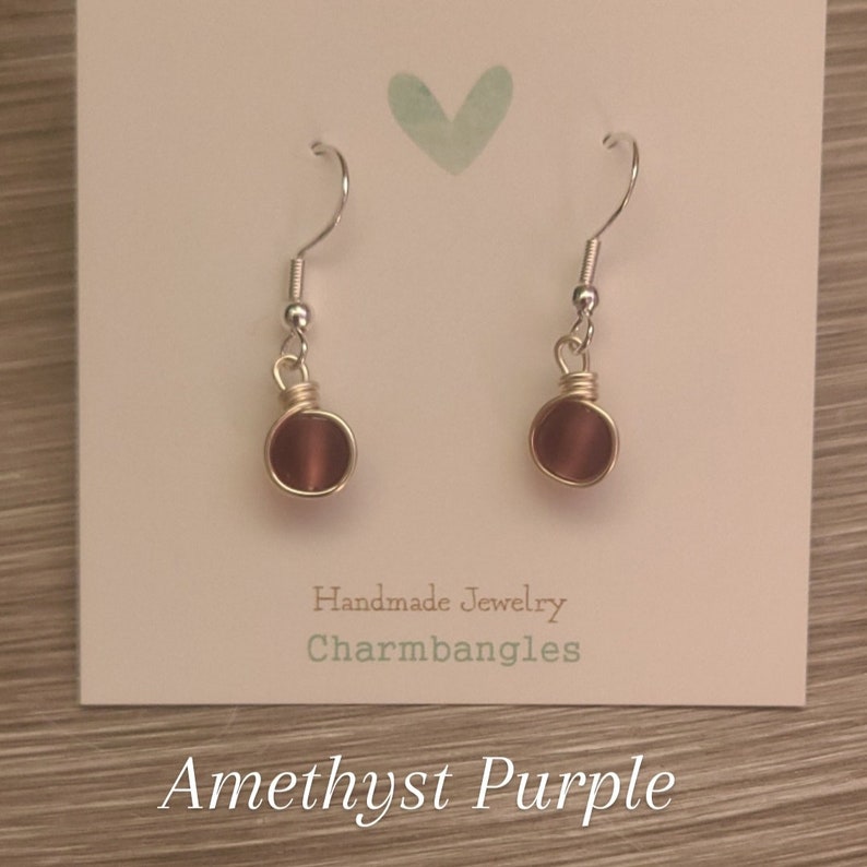 May include: Amethyst purple earrings with silver hooks and gold wire wrapped around the stone.
