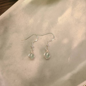 May include: A pair of silver dangle earrings with light blue round stones.