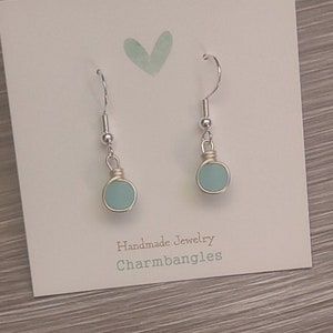 May include: A pair of frosted blue glass earrings with silver hooks. The earrings are handmade by Charmbangles.
