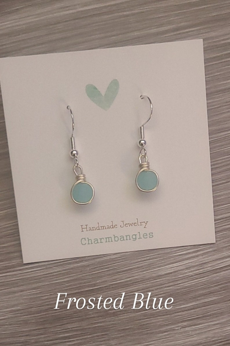 May include: A pair of frosted blue glass earrings with silver hooks. The earrings are handmade by Charmbangles.